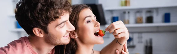 Улыбающийся мужчина кормит девушку свежей клубникой, плакатом — стоковое фото