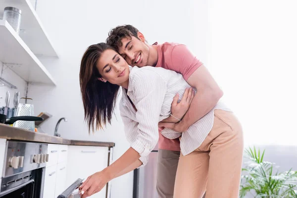 Smiling man hugging girlfriend near open oven in kitchen — Stock Photo