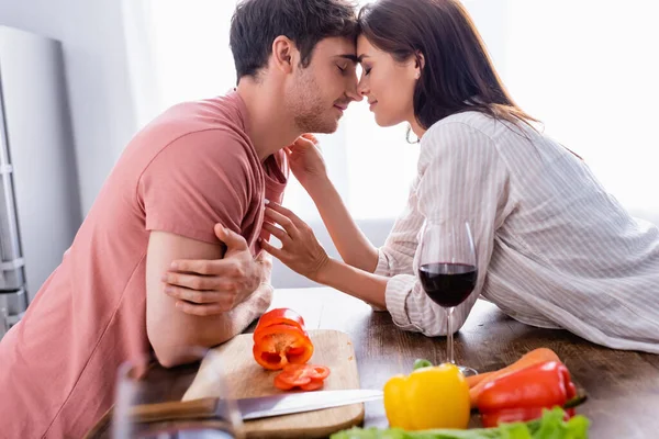 Jeune femme touchant petit ami près du vin et des légumes frais au premier plan flou — Photo de stock