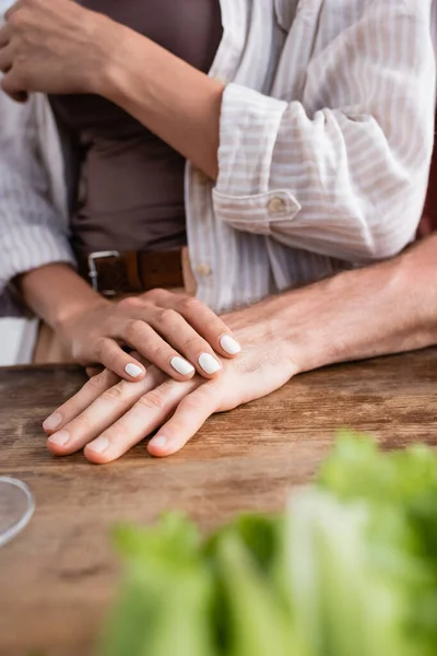 Vista cortada da mulher segurando a mão namorado na mesa da cozinha em primeiro plano desfocado — Fotografia de Stock
