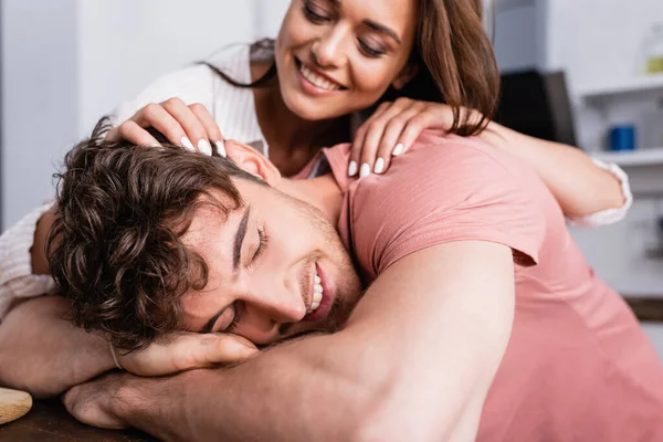 Sonriente hombre con los ojos cerrados cerca de la novia sobre fondo borroso en la cocina - foto de stock