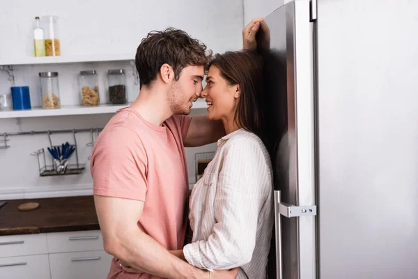 Smiling couple kissing near fridge in kitchen — Stock Photo