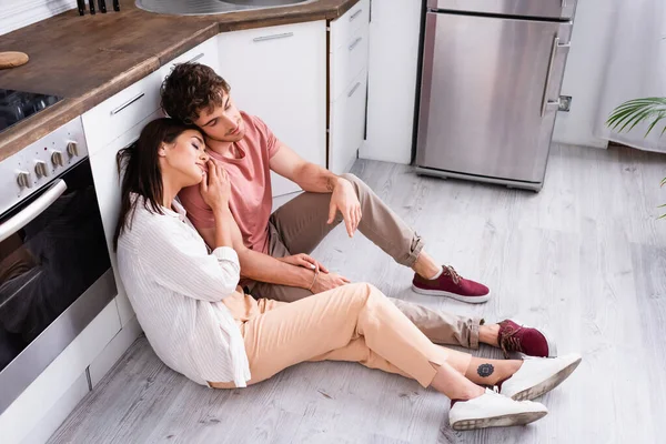 Pareja joven con los ojos cerrados sentados en el suelo en la cocina - foto de stock