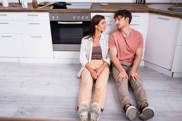 Junges Paar schaut einander an, während es auf dem Fußboden in der Küche sitzt — Stockfoto