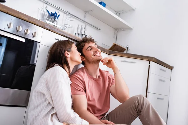 Mujer joven sentada cerca de hombre sonriente en la cocina — Stock Photo