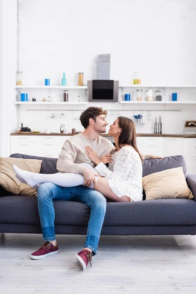 Pareja sonriente mirándose mientras están sentados en el sofá en casa - foto de stock