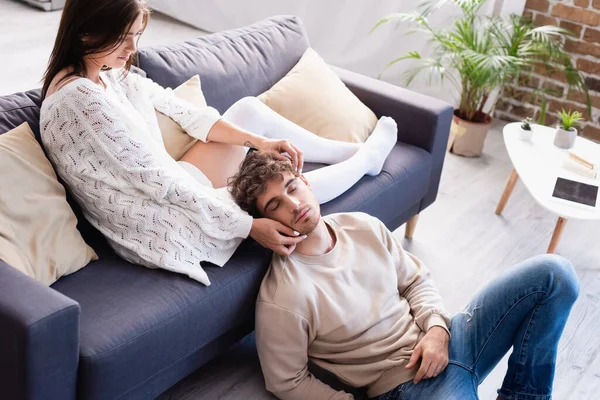 Mujer joven tocando la cara del novio mientras se sienta en el sofá en casa - foto de stock
