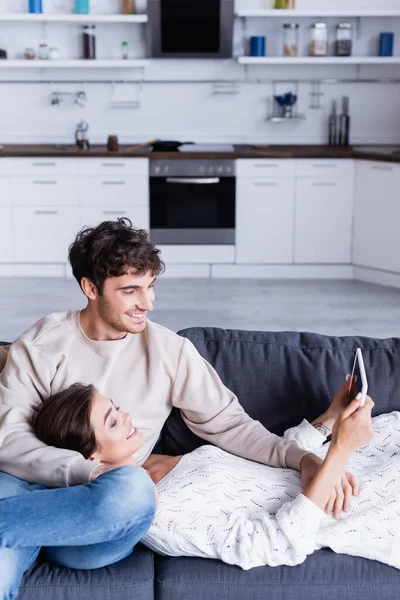 Pareja sonriente usando tableta digital con pantalla en blanco en el sofá en casa - foto de stock