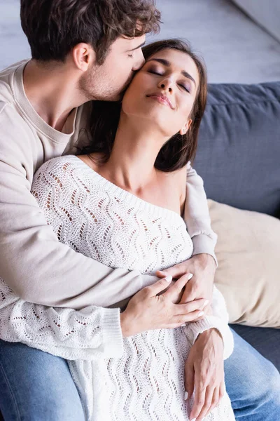 Hombre besando morena novia en jersey de punto en la sala de estar - foto de stock