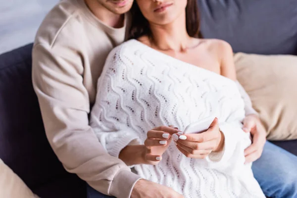 Cropped view of woman using smartphone near boyfriend on blurred background on couch — Stock Photo