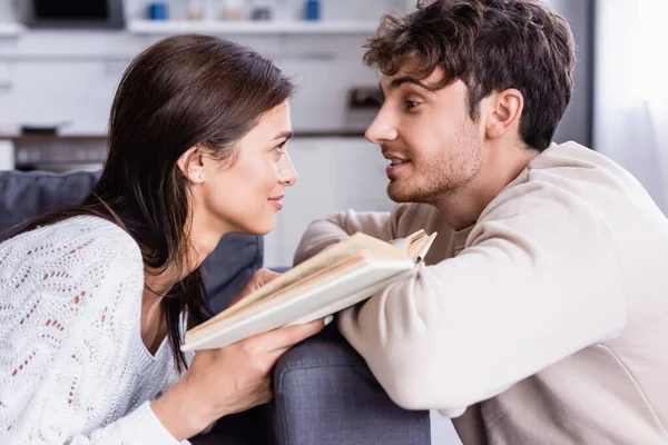 Lächelnde Frau mit Buch schaut Freund zu Hause an — Stockfoto