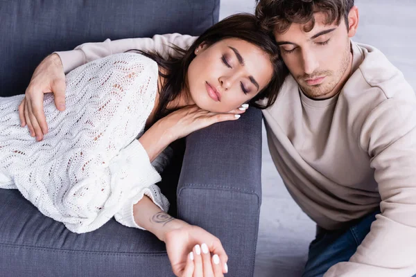 Junger Mann umarmt brünette Freundin mit geschlossenen Augen auf Couch — Stockfoto