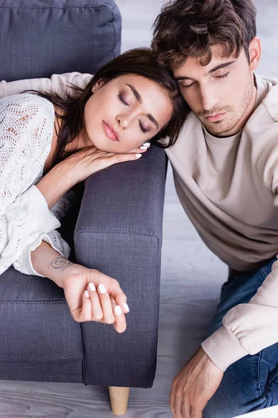 Young woman with closed eyes lying on couch near boyfriend at home — Stock Photo