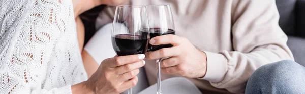 Cropped view of glasses of red wine in hands of young couple on blurred background, banner — Stock Photo