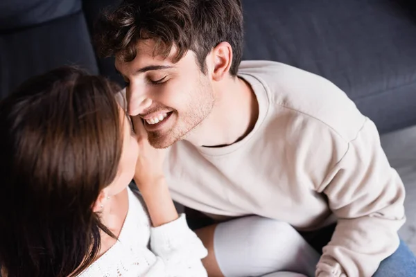 Vista aérea del hombre sonriente mirando a la novia morena en el sofá - foto de stock