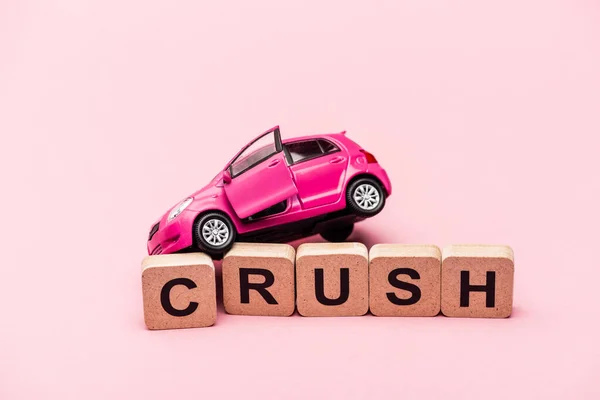 Іграшковий автомобіль і слово розчавити на кубиках на рожевому фоні — стокове фото