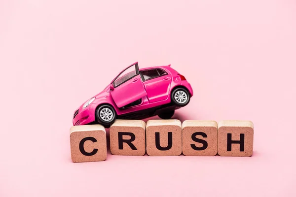 Toy car and word crush on cubes on pink background — Stock Photo