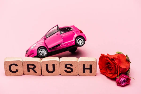 Rosas, coche de juguete y palabra aplastamiento en cubos sobre fondo rosa - foto de stock