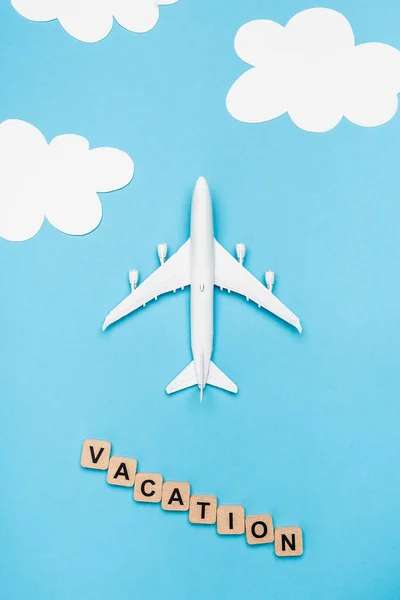 Top view of plane model and cubes with word vacation on blue sky background — Stock Photo