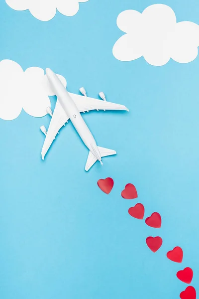 Top view of plane model and red hearts on blue background with white clouds — Stock Photo