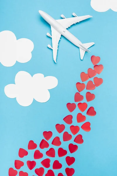 Draufsicht auf Flugzeugmodell und rote Herzen auf blauem Hintergrund mit weißen Wolken — Stockfoto