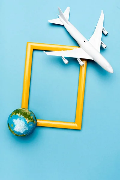 Top view of white plane model, globe and empty frame on blue background — Stock Photo