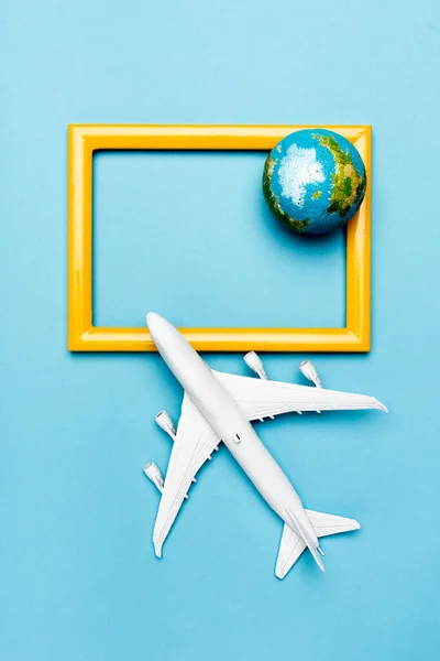 Top view of white plane model, globe and empty frame on blue background — Stock Photo