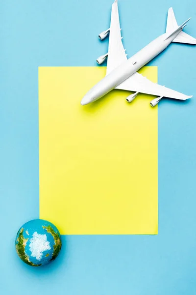 Draufsicht auf weißes Flugzeugmodell, Globus und leeres gelbes Papier auf blauem Hintergrund — Stockfoto