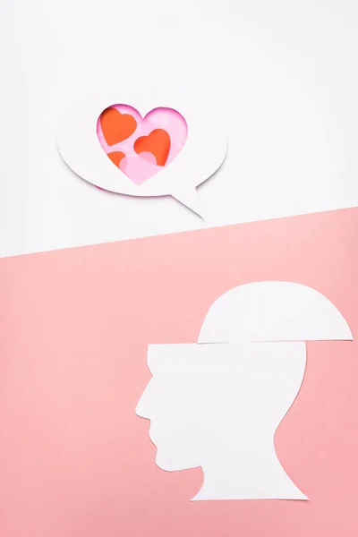 Vista superior de la burbuja del habla con corazones y cabeza humana sobre fondo blanco y rosa - foto de stock