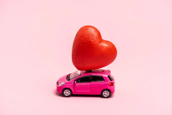 Toy car and red heart on pink background — Stock Photo