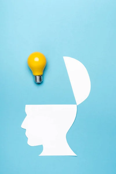 Top view yellow light bulb and paper human head on blue background — Stock Photo