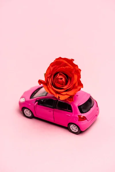 Carro de brinquedo e rosa vermelha no fundo rosa — Fotografia de Stock