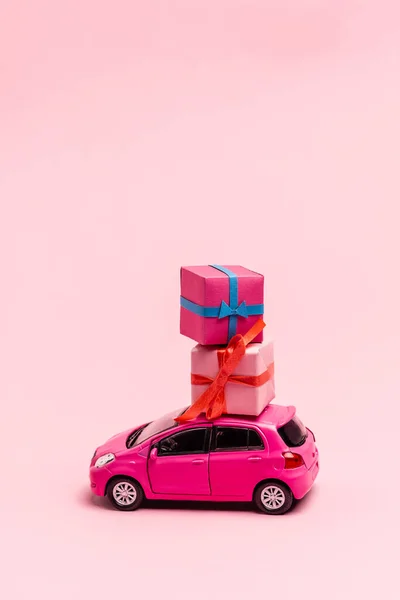 Carro de brinquedo e caixas de presente no fundo rosa — Fotografia de Stock