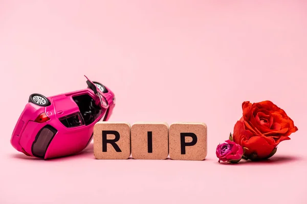 Crashed car and word rip with flowers on pink background — Stock Photo