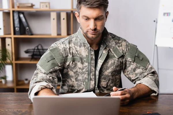 Soldado de uniforme sentado na mesa e usando laptop — Fotografia de Stock