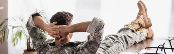 Вид ззаду солдата у військовій формі, що відпочиває в офісі, банер — стокове фото