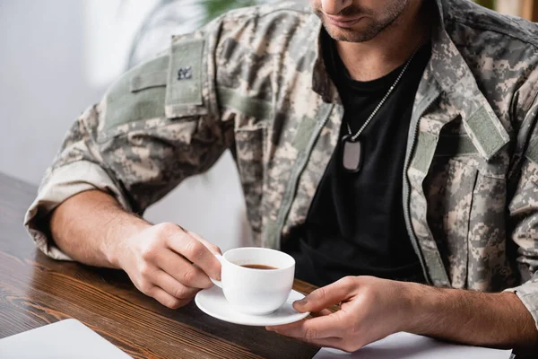 Vista recortada del militar en uniforme sosteniendo taza de café y platillo en la oficina - foto de stock