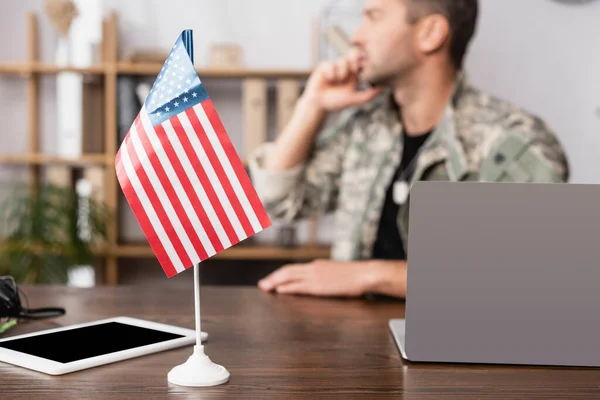 Bandera americana y tableta digital con pantalla en blanco cerca de militar en uniforme sobre fondo borroso - foto de stock