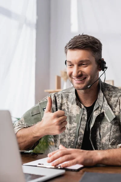 Військовий чоловік у формі та гарнітурі показує великий палець вгору біля ноутбука — Stock Photo