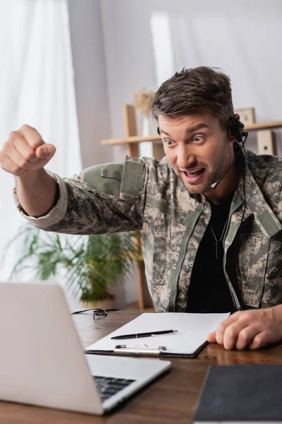 Uomo militare in uniforme e auricolare con pugno serrato guardando computer portatile — Foto stock