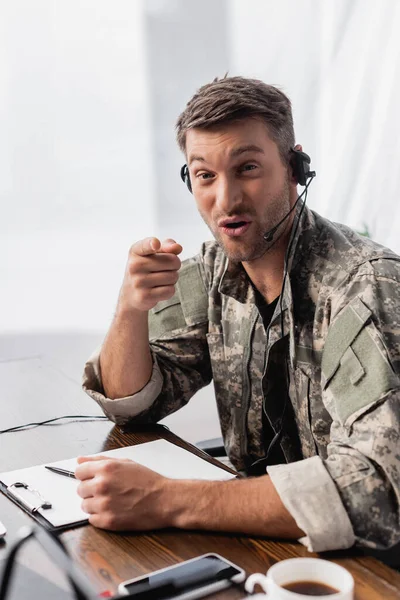 Militar homem de uniforme e fone de ouvido falando enquanto apontando com o dedo — Fotografia de Stock