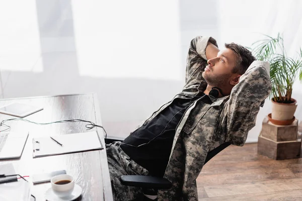 Солдат у військовій формі та гарнітурі, що відпочиває біля гаджетів на стільці — стокове фото