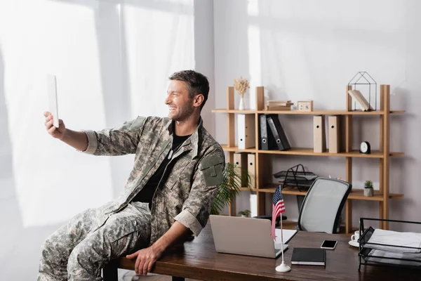 Soldado feliz en uniforme militar usando tableta digital mientras tiene video chat en la oficina - foto de stock