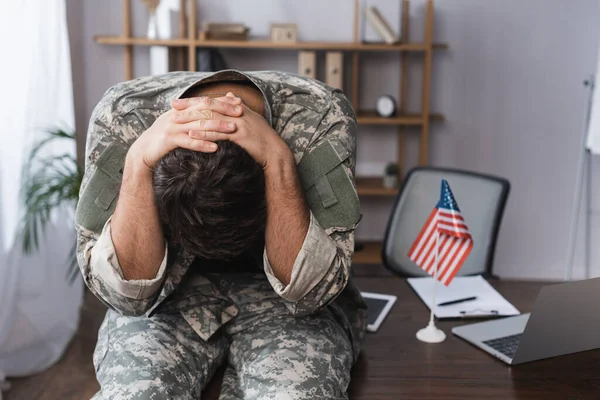 Militar homem sentado na mesa e inclinando-se perto de gadgets e bandeira americana — Fotografia de Stock