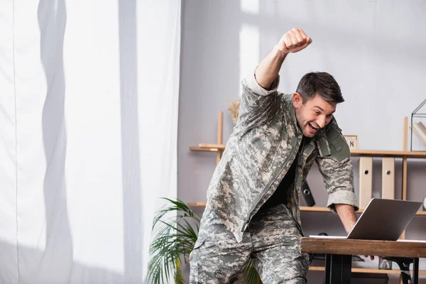 Homem militar animado com punho cerrado regozijando-se ao usar laptop — Fotografia de Stock