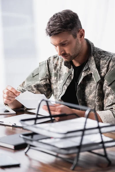 Military man in uniform holding envelope with letter near document tray on blurred foreground — Stock Photo