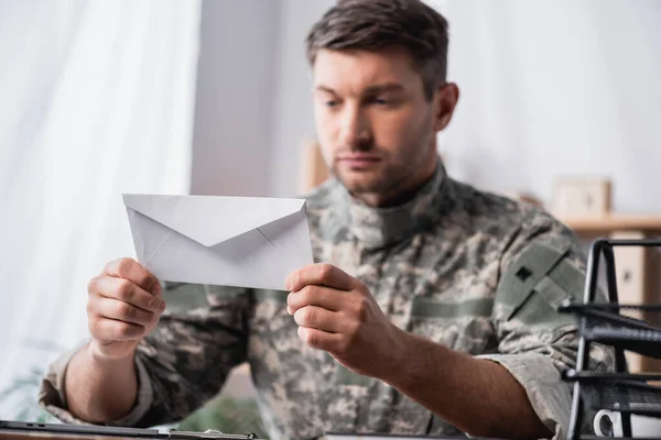 White envelope in hands of soldier on blurred background — Stock Photo