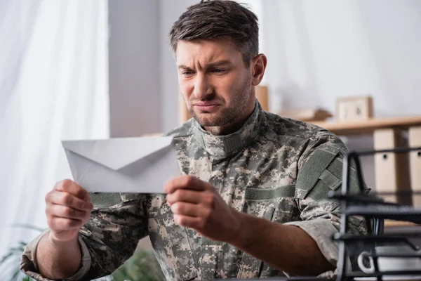 Weißer Umschlag in den Händen eines unzufriedenen Soldaten auf verschwommenem Hintergrund — Stockfoto