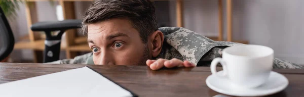 Uomo militare spaventato nascosto sotto la scrivania, striscione — Foto stock