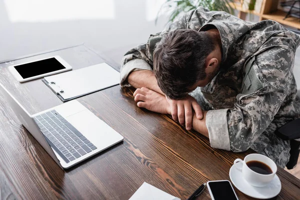 Militärmann in Uniform liegt auf Schreibtisch neben Laptop und Gerät mit leerem Bildschirm — Stockfoto